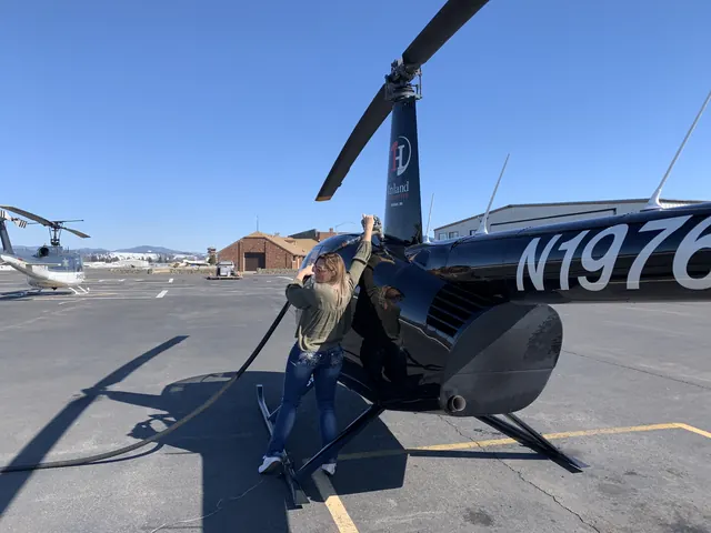Amy Hartt performing a preflight check on a black Robinson helicopter on a sunny ramp.